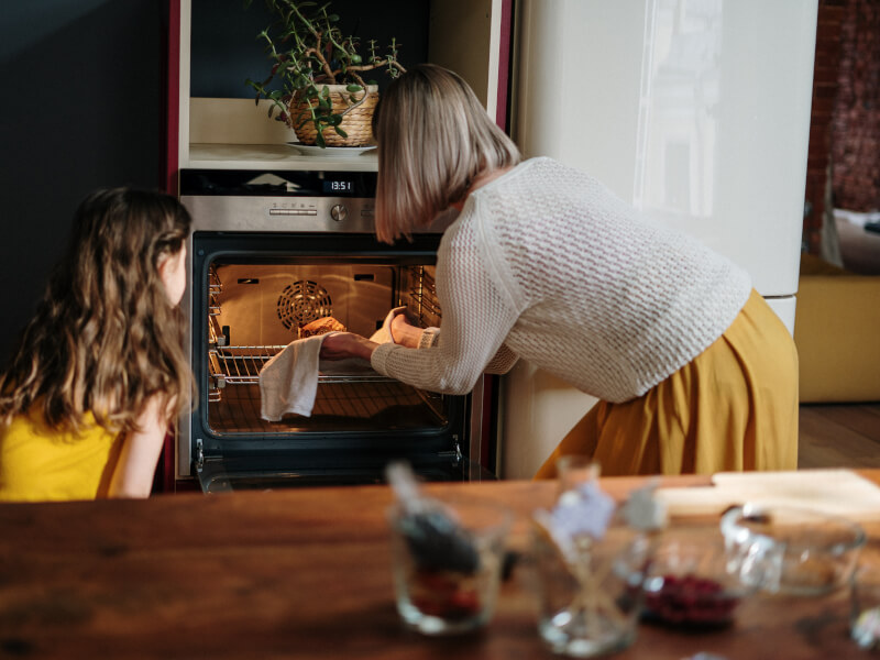 A woman and child put food in the oven to cook